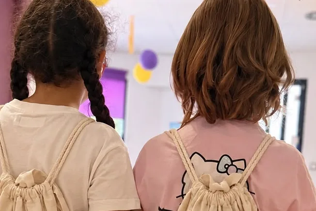 Dos niñas de espaldas, con sus mochilas, en la entrada de la academia