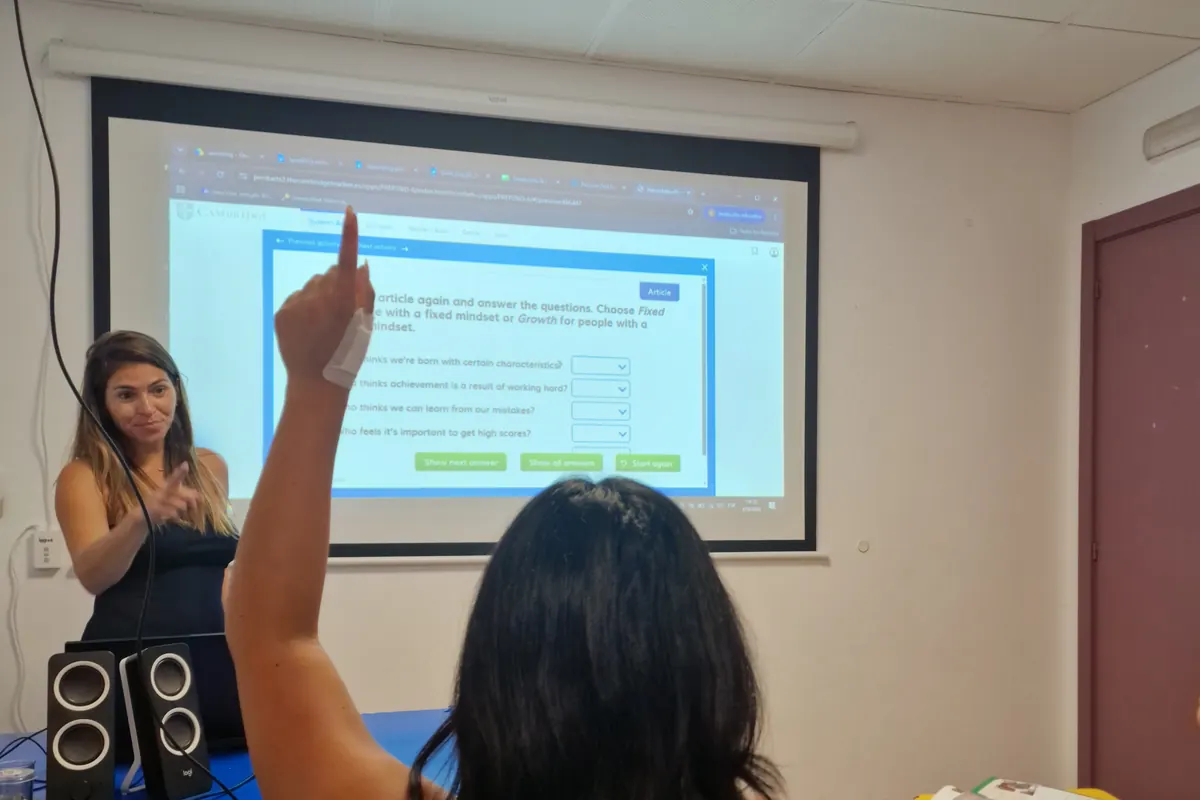 Alumna levantando la mano en una clase de preparación de exámenes Cambridge