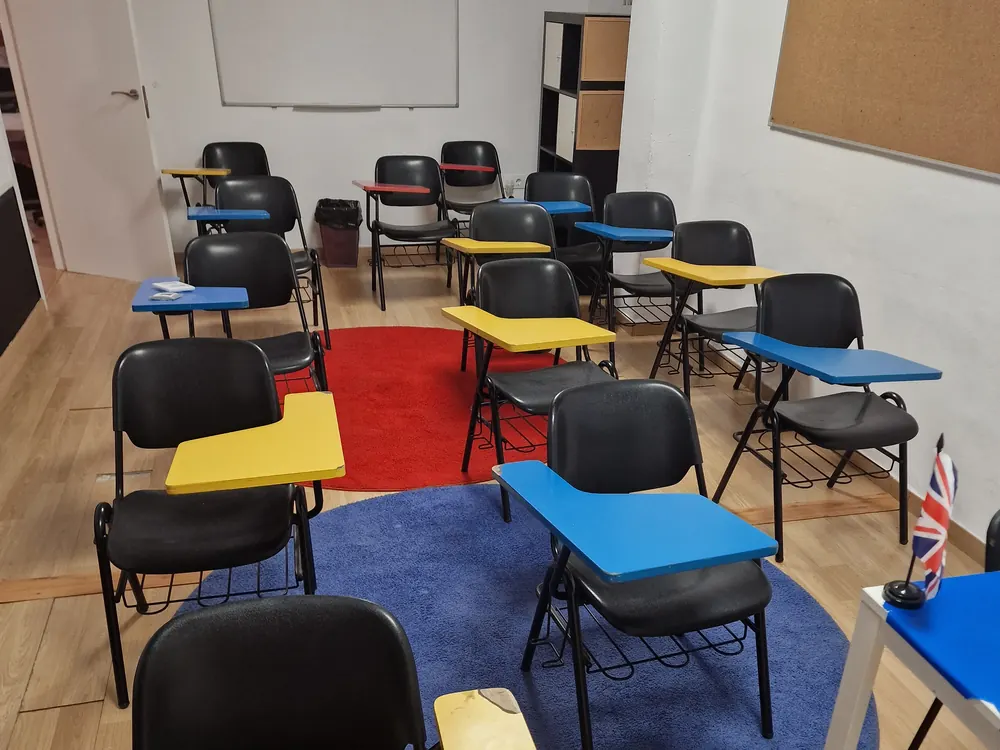 Aula con sillas de pala de colores, pizarra y alfombras