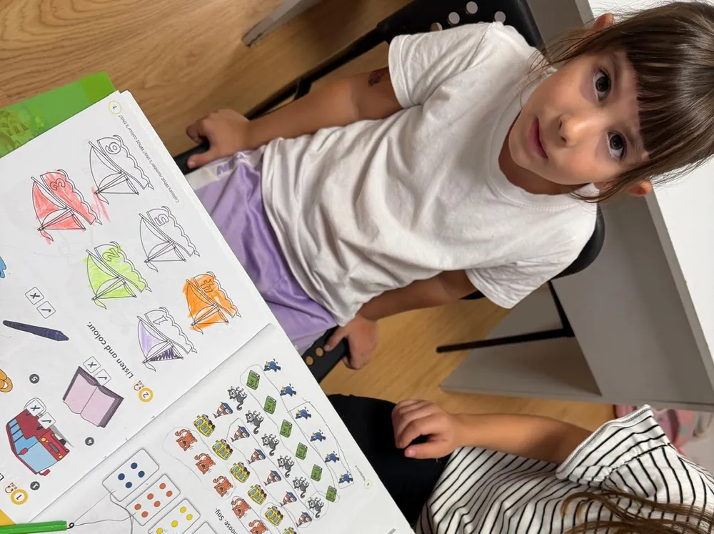 Niña sonriendo con su cuaderno de actividades abierto sobre la mesa