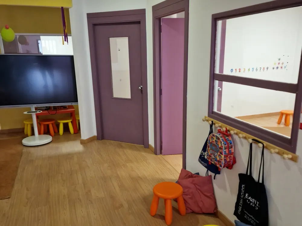 Zona de entrada de la academia con pantalla, percheros y taburetes de colores