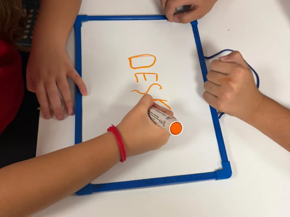 Manos de niños escribiendo una palabra en inglés en una pizarra pequeña