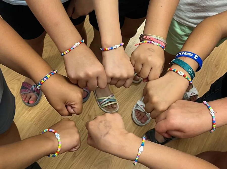 Niños y niñas juntando los puños en un corro, con pulseras de colores